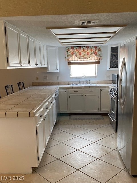kitchen featuring white cabinets, stainless steel appliances, a sink, visible vents, and tile counters