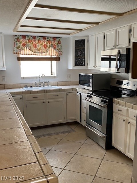 kitchen with white cabinets, a sink, tile countertops, and appliances with stainless steel finishes