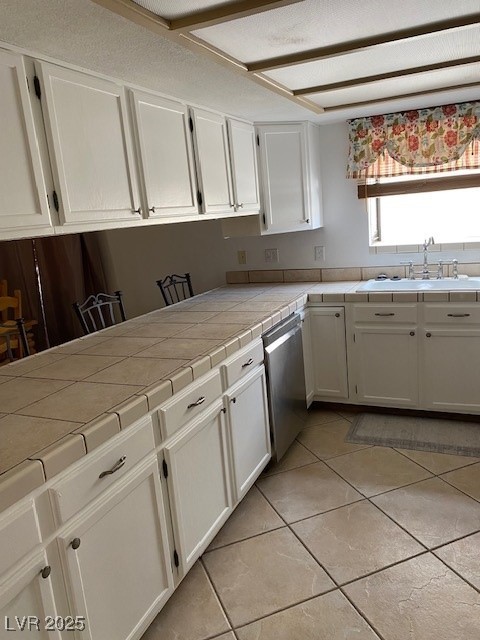 kitchen with stainless steel dishwasher, a sink, white cabinetry, tile counters, and light tile patterned floors