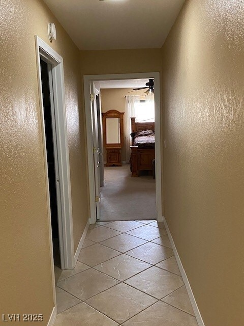 hall with baseboards, light tile patterned flooring, and a textured wall