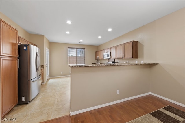 10664 Mount Jefferson Ave, Las Vegas, NV 89166 - kitchen featuring stainless steel appliances, a peninsula, light stone countertops, recessed lighting, and baseboards