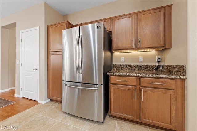 10664 Mount Jefferson Ave, Las Vegas, NV 89166 - kitchen featuring freestanding refrigerator, brown cabinetry, dark stone countertops, and baseboards