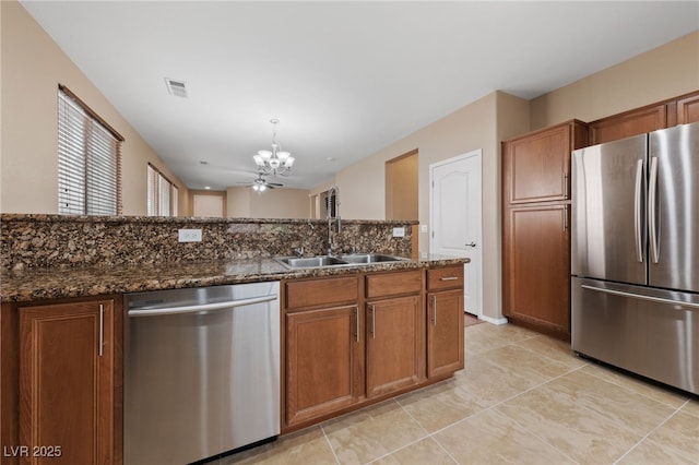 10664 Mount Jefferson Ave, Las Vegas, NV 89166 - kitchen with appliances with stainless steel finishes, a sink, a chandelier, brown cabinets, and dark stone countertops
