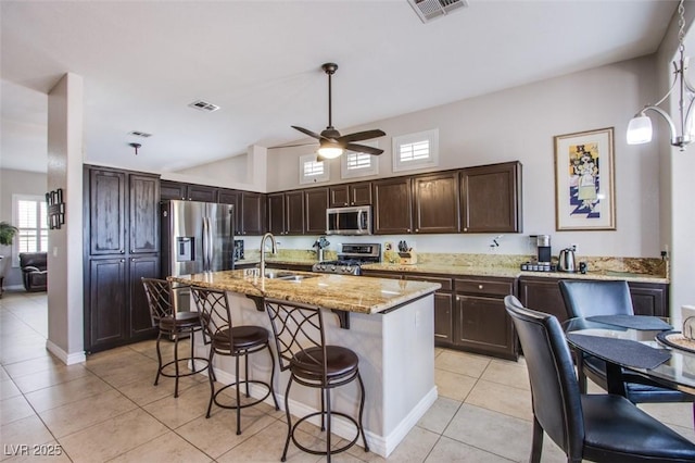 1552 Livingston Dr, Henderson, NV 89012 - kitchen featuring stainless steel appliances, light tile patterned floors, dark brown cabinets, a kitchen bar, and light stone countertops