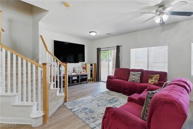 living area with stairway, a ceiling fan, and wood finished floors
