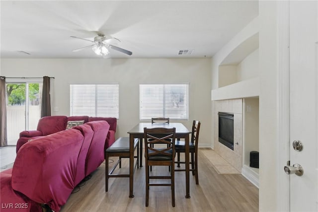 dining area with baseboards, visible vents, light wood-style floors, a ceiling fan, and a fireplace