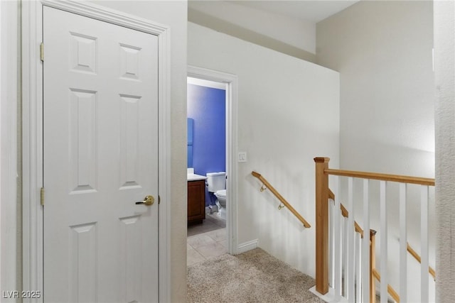 hallway featuring light tile patterned floors, an upstairs landing, and light colored carpet