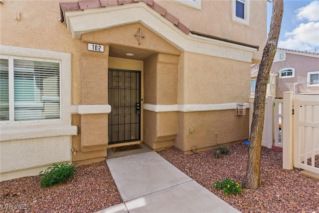 property entrance featuring a gate, stucco siding, and fence