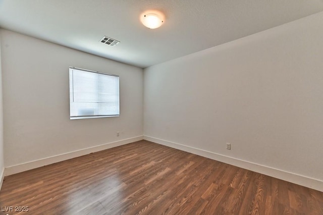 spare room featuring baseboards, visible vents, and dark wood-style flooring