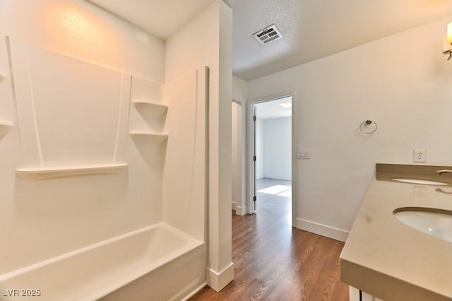 full bathroom with bathing tub / shower combination, wood finished floors, visible vents, a sink, and baseboards