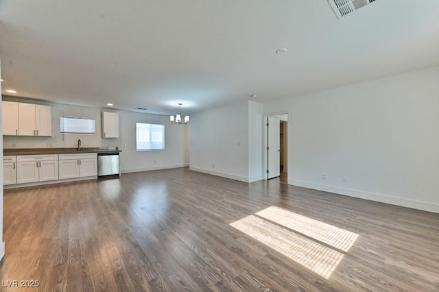 unfurnished living room featuring a sink, baseboards, visible vents, a notable chandelier, and wood finished floors