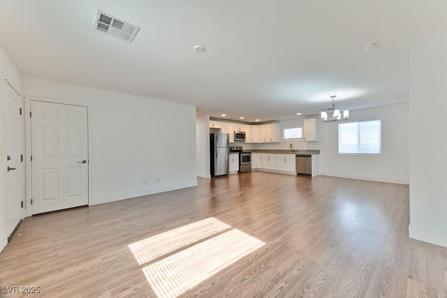 unfurnished living room featuring baseboards, light wood-style flooring, visible vents, and a chandelier