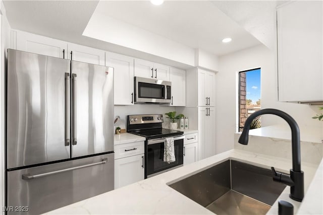 kitchen featuring white cabinets, light stone countertops, stainless steel appliances, and a sink