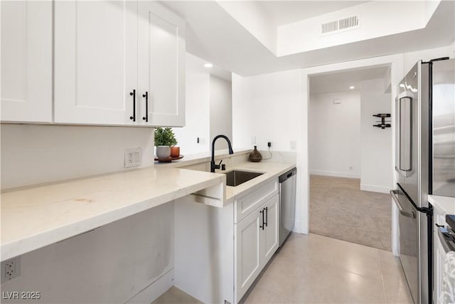 kitchen with a sink, light colored carpet, white cabinets, appliances with stainless steel finishes, and visible vents