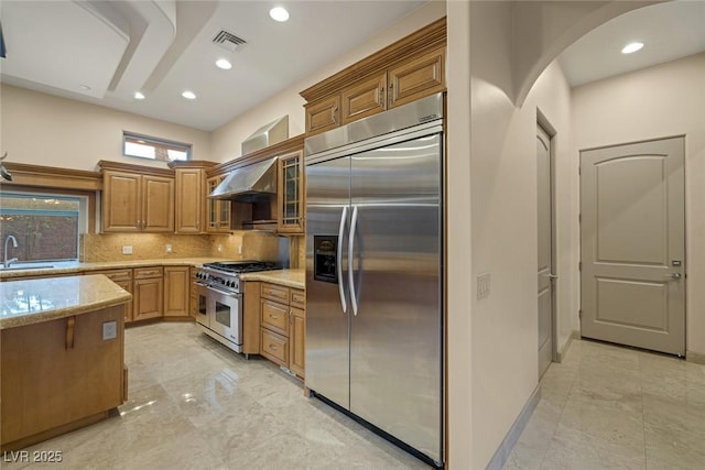 1665 Liege Dr, Henderson, NV 89012 - kitchen featuring brown cabinets, stainless steel appliances, visible vents, wall chimney range hood, and light stone countertops