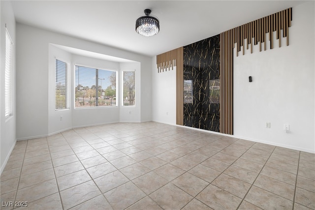 empty room featuring tile patterned floors, baseboards, and an inviting chandelier