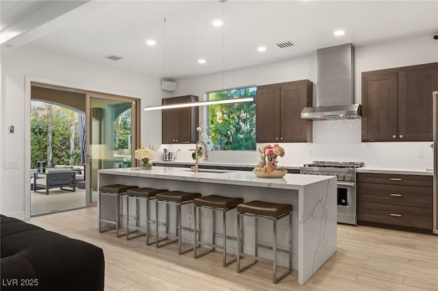 kitchen featuring high end range, wall chimney exhaust hood, a breakfast bar, and visible vents