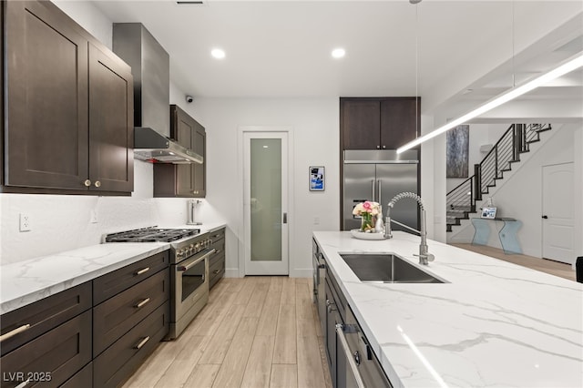 kitchen featuring premium appliances, a sink, extractor fan, dark brown cabinetry, and light wood-style flooring