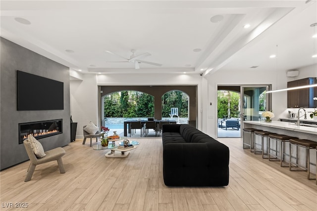 living area with light wood-style floors, plenty of natural light, a ceiling fan, and a large fireplace
