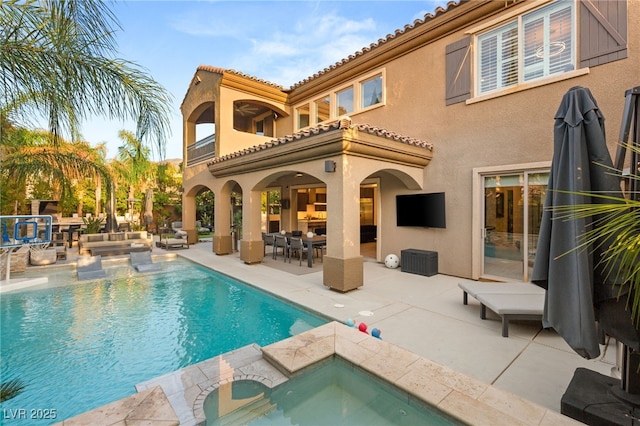 back of house with a tile roof, a patio area, an outdoor hangout area, a pool with connected hot tub, and stucco siding