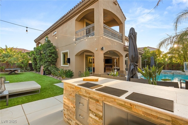 view of front of property with exterior kitchen, a patio area, a balcony, a front yard, and stucco siding