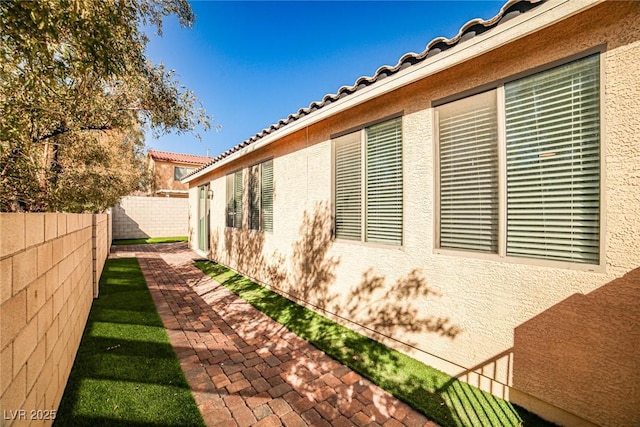 view of side of home featuring a patio area, a tiled roof, a fenced backyard, and stucco siding