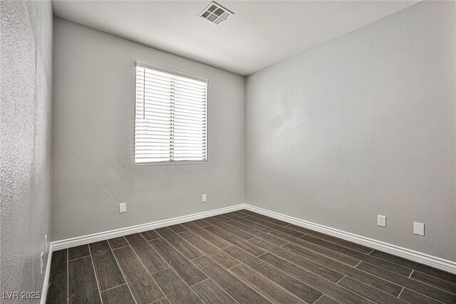 spare room featuring baseboards, dark wood-style flooring, and visible vents