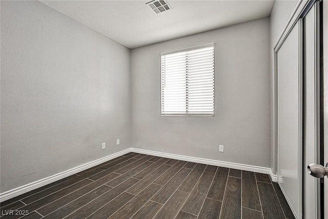unfurnished bedroom featuring baseboards, dark wood-style flooring, visible vents, and a closet