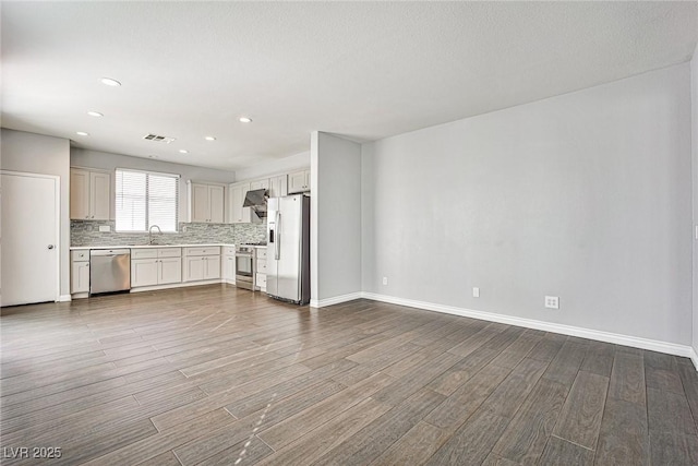 unfurnished living room featuring wood finished floors, visible vents, baseboards, and a sink