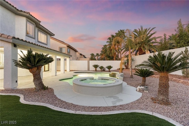 yard at dusk featuring a patio, a fenced backyard, and an in ground hot tub