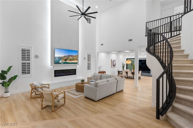 living room with a glass covered fireplace, light wood-style flooring, a high ceiling, and stairs