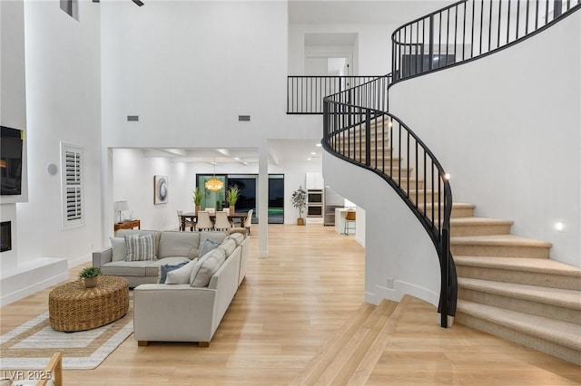 living room with stairs, a towering ceiling, visible vents, and light wood-style floors
