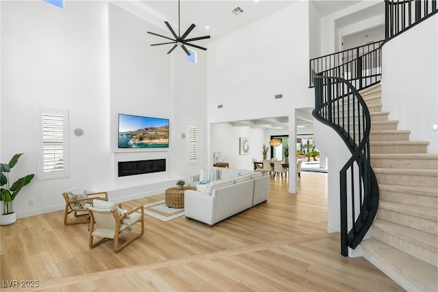 living area featuring a high ceiling, visible vents, a glass covered fireplace, light wood-style flooring, and stairs
