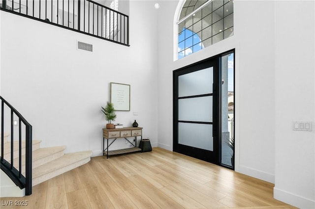 foyer featuring stairway, wood finished floors, baseboards, a high ceiling, and visible vents