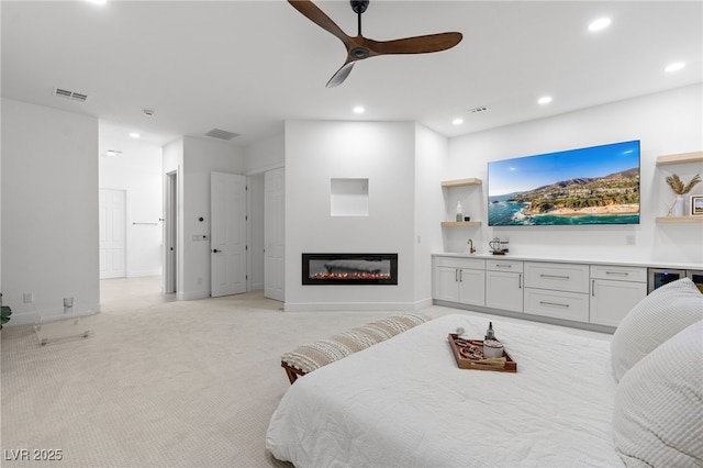 bedroom featuring light carpet, a glass covered fireplace, visible vents, and recessed lighting