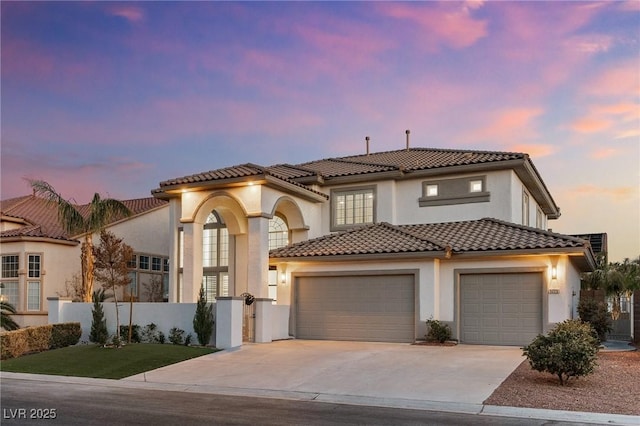 mediterranean / spanish home featuring a tile roof, concrete driveway, fence, a garage, and stucco siding