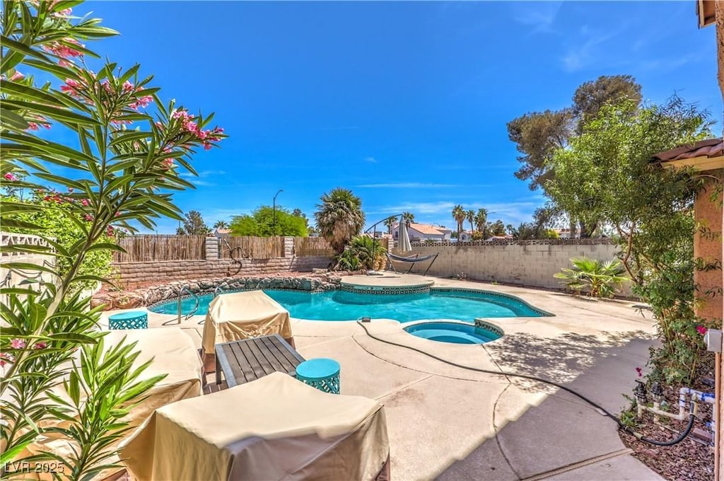 view of pool with a fenced backyard, a pool with connected hot tub, and a patio
