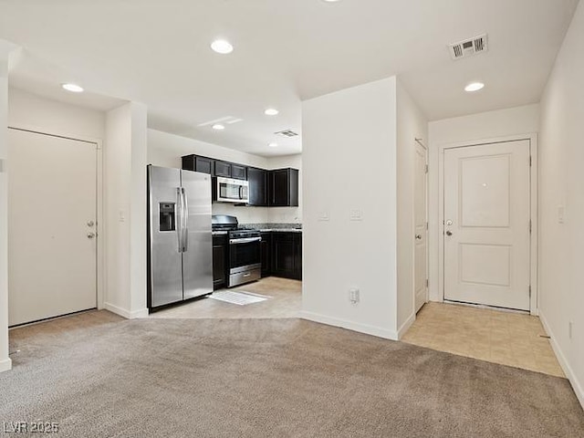 kitchen with stainless steel appliances, dark cabinetry, visible vents, light carpet, and baseboards
