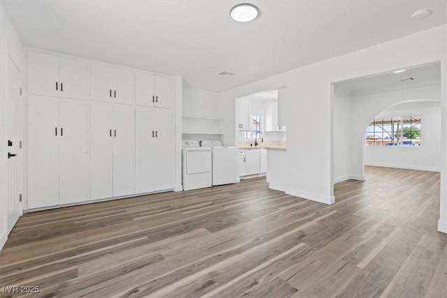 429 N 10th St, Las Vegas, NV 89101 - unfurnished living room with washer and clothes dryer, light wood-style flooring, arched walkways, baseboards, and a sink