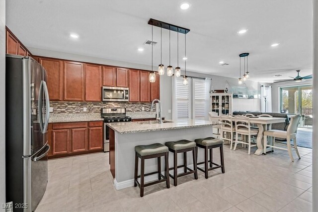 kitchen featuring a ceiling fan, tasteful backsplash, light stone counters, brown cabinetry, and appliances with stainless steel finishes