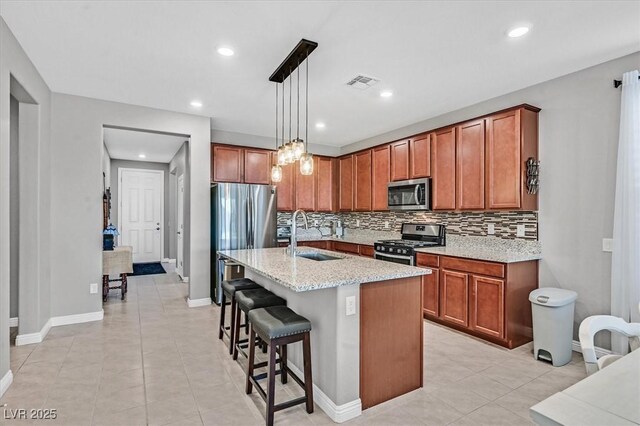 kitchen featuring stainless steel appliances, a sink, tasteful backsplash, visible vents, and brown cabinets