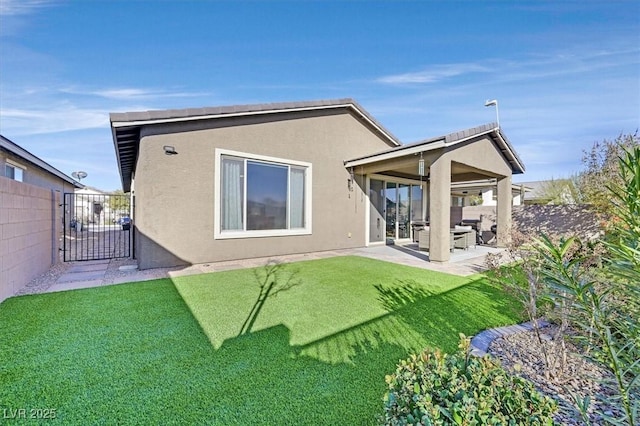 back of house featuring a gate, fence, a yard, stucco siding, and a patio