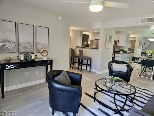 living area featuring ceiling fan, baseboards, visible vents, and light wood-type flooring