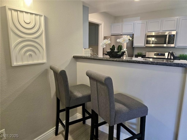 kitchen with stainless steel appliances, dark stone counters, baseboards, a kitchen bar, and wood finished floors