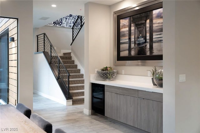 bar featuring light wood-style flooring, baseboards, beverage cooler, and stairs