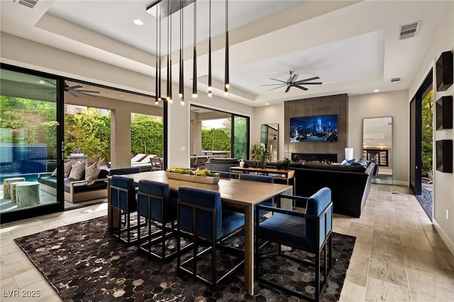 dining space featuring a tray ceiling, a tile fireplace, visible vents, and a ceiling fan