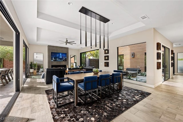 dining area with ceiling fan, a large fireplace, a tray ceiling, and visible vents
