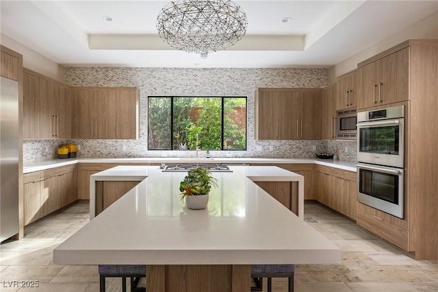 kitchen with light countertops, a center island, a tray ceiling, and appliances with stainless steel finishes