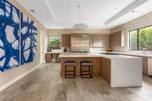 kitchen with stainless steel appliances, a sink, a large island, visible vents, and light countertops