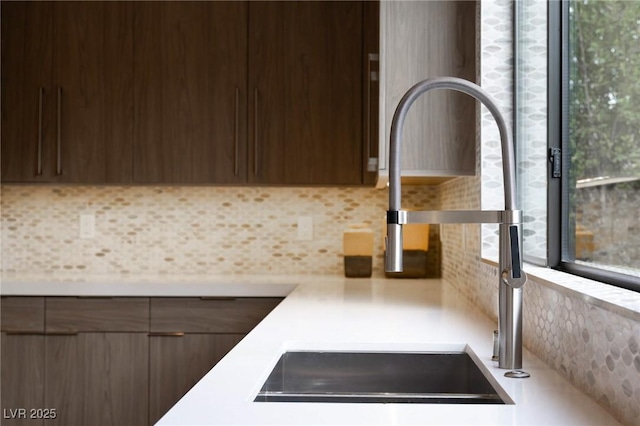room details with light countertops, a sink, modern cabinets, dark brown cabinetry, and decorative backsplash